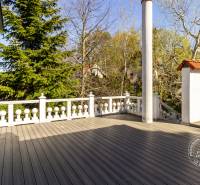 Terasz fa dekorációjú padlóval, környező zöld növényzettel és erkélykorláttal.