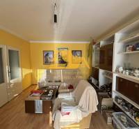 Nappali egy családi házban fehér kanapéval, fa mintázatú padlóval, sárga falakkal.