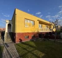 Sárga családi ház Érsekújváron, rendezett kerttel és járdával az utcán.