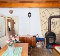 Családi ház belső tere cserépkályhával, fából készült mennyezettel és virágokkal díszített étkezőasztallal.