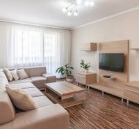 Nappali egy háromszobás lakásban kanapéval, televízióval és fa dekorációjú padlóval.