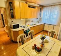 Konyha egy háromszobás lakásban, fa dekor padlóval és étkezőasztallal.