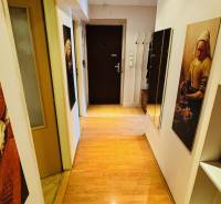 Keskeny folyosó fa mintázatú padlóval egy háromszobás lakásban, képekkel és tükörrel.