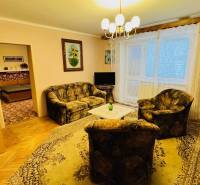 Nappali egy háromszobás lakásban kanapéval, fotellel és fa dekorációjú padlóval.