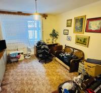 Nappali egy háromszobás lakásban dekorációkkal, bútorokkal és fa mintázatú padlóval.