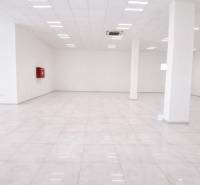 Tágas üzlethelyiségek fehér padlóval és oszlopokkal, világos világítással.