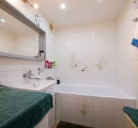 Fürdőszoba egy háromszobás lakásban káddal, mosdóval és fehér csempével.