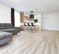 Nappali egy háromszobás lakásban kanapéval, bárral és fa dekorációjú padlóval.