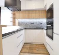 Konyha egy háromszobás lakásban fehér szekrényekkel és fa dekor padlóval.