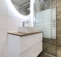 Fürdőszoba mosdóval és zuhanyzóval egy háromszobás lakásban, fa dekoros padlóval.