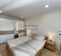 Világos hálószoba egy egyszobás lakásban, fa dekor padlóval és beépített szekrénnyel.