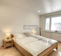 Világos hálószoba egy egyszobás lakásban, fa dekoros padlóval és nagy ablakkal.