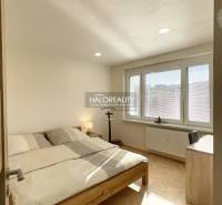 Hálószoba egy egyszobás lakásban fa mintázatú padlóval és nagy ablakokkal.