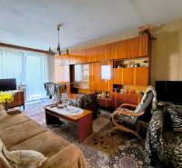 Nappali egy háromszobás lakásban rusztikus bútorokkal és feltűnő szőnyeggel.