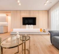 Nappali egy háromszobás lakásban, fa dekoros padlóval és falra szerelt televízióval.