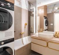 Fürdőszoba egy háromszobás lakásban káddal, mosdóval, szárítóval és elegáns arany kiegészítőkkel.