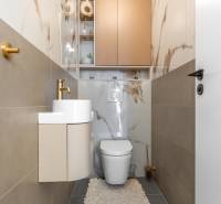 WC mosdókagylóval, arany csaptelep és márványmintás csempe egy háromszobás lakásban.