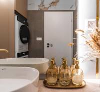 Fürdőszoba mosdóval, arany adagolókkal és dekoratív természetes díszítéssel egy háromszobás lakásban.