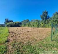 Lakótelek Hosťovában kerítéssel és környező zöldterülettel a kék ég alatt.