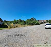 Telkek - lakhatás Hosťovában: kavicsos út, bekerített telek, mellette parkoló autó.