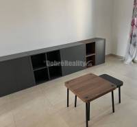 Nappali egy kétszobás lakásban, járólappal, asztallal és sötét szekrénnyel.