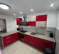 Konyha piros szekrényekkel és fa dekor padlóval egy kétszobás lakásban.