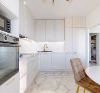 Konyha egy háromszobás lakásban fehér szekrényekkel és kőpadlóval.