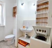 Fürdőszoba egy kétszobás lakásban mosógéppel, szaniterrel és törölközőtartó polccal.