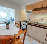 Konyha egy kétszobás lakásban ülősarokkal, világos padlóval és étkezőasztallal.