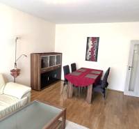 Nappali kanapéval, étkezőasztallal és fa dekorációjú padlóval egy háromszobás lakásban.