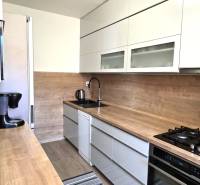 Konyha egy háromszobás lakásban fa dekorációjú konyhapulttal és padlóval.