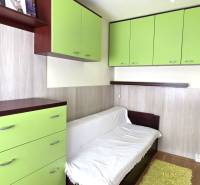 Szoba egy háromszobás lakásban fehér kanapéval, zöld szekrényekkel és fa dekoros padlóval.