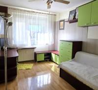 Nappali kanapéval, polcokkal és asztallal egy háromszobás lakásban, fa dekorációjú padlóval.