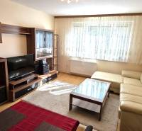 Nappali bézs kanapéval és sötét fa bútorokkal egy háromszobás lakásban.