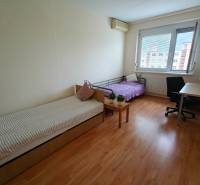 Szoba egy háromszobás lakásban két ággyal, íróasztallal és fa dekorációjú padlóval.