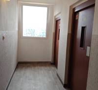 Liftfolyosó és fa mintázatú padló egy háromszobás lakásban.