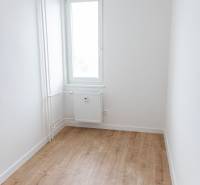 Szoba egy háromszobás lakásban, ablakkal és fa mintázatú padlóval.