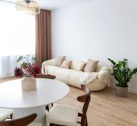 3 szobás lakás belső tere krémszínű kanapéval, növénnyel és asztallal fa dekorációjú padlón.