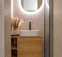 Fürdőszoba egy háromszobás lakásban, mosdókagylóval egy fa szekrényen és világítással ellátott tükörrel.