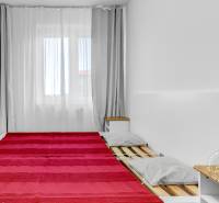 Hálószoba egy kétszobás lakásban, ággyal, szürke párnákkal, takaróval és éjjeliszekrénnyel.