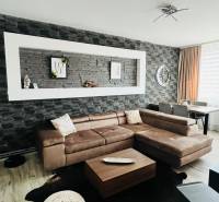 Nappali egy háromszobás lakásban, fa mintázatú padlóval és sarok ülőgarnitúrával.