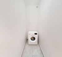 Keskeny helyiség mosógéppel egy kétszobás lakásban, fehér falak, csempe a padlón.