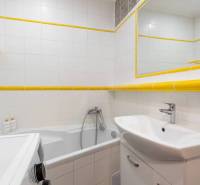 A nyaraló apartman fürdőszobája káddal, mosdóval, mosógéppel és fehér csempékkel.