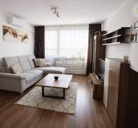 Nappali egy négy szobás lakásban, fa mintázatú padlóval, kanapéval és televízióval.