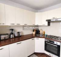 Konyha egy 4 szobás lakásban fehér szekrényekkel és fa hatású padlóval.