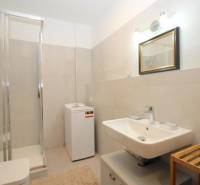 Fürdőszoba mosdóval, mosógéppel és zuhanyzóval egy egyszobás lakásban.