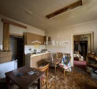 Konyha egy családi házban, fa bútorokkal, régi televízióval, étkezőasztallal és szekrénnyel.