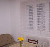 Szoba kanapéval, asztallal, székkel és függönnyel, az asztalon egy váza virágokkal.