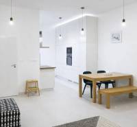 Egy 2 szobás lakás belső tere fehér falakkal, fa asztallal és fekete kanapéval.