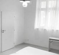 Fehér szoba franciaággyal, asztallal és függőlámpával egy kétszobás lakásban.